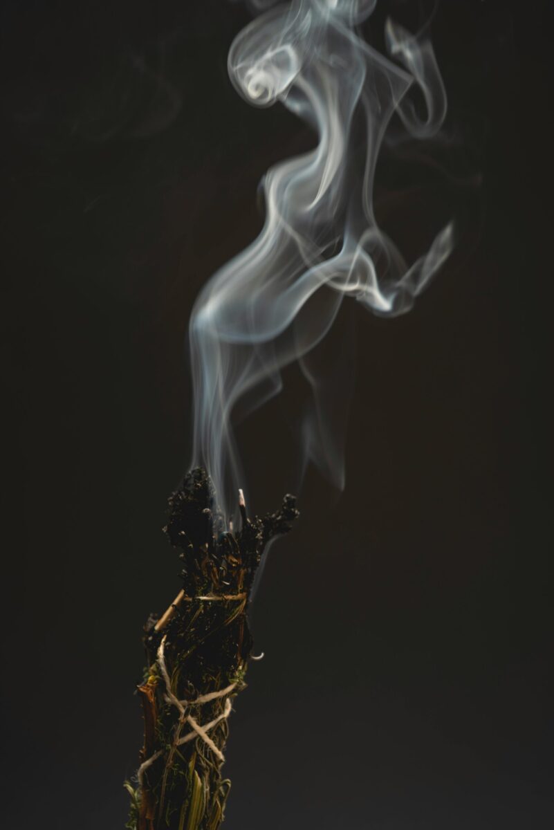 Ethereal smoke swirls from burning incense, creating a mystical ambiance against a dark background.
